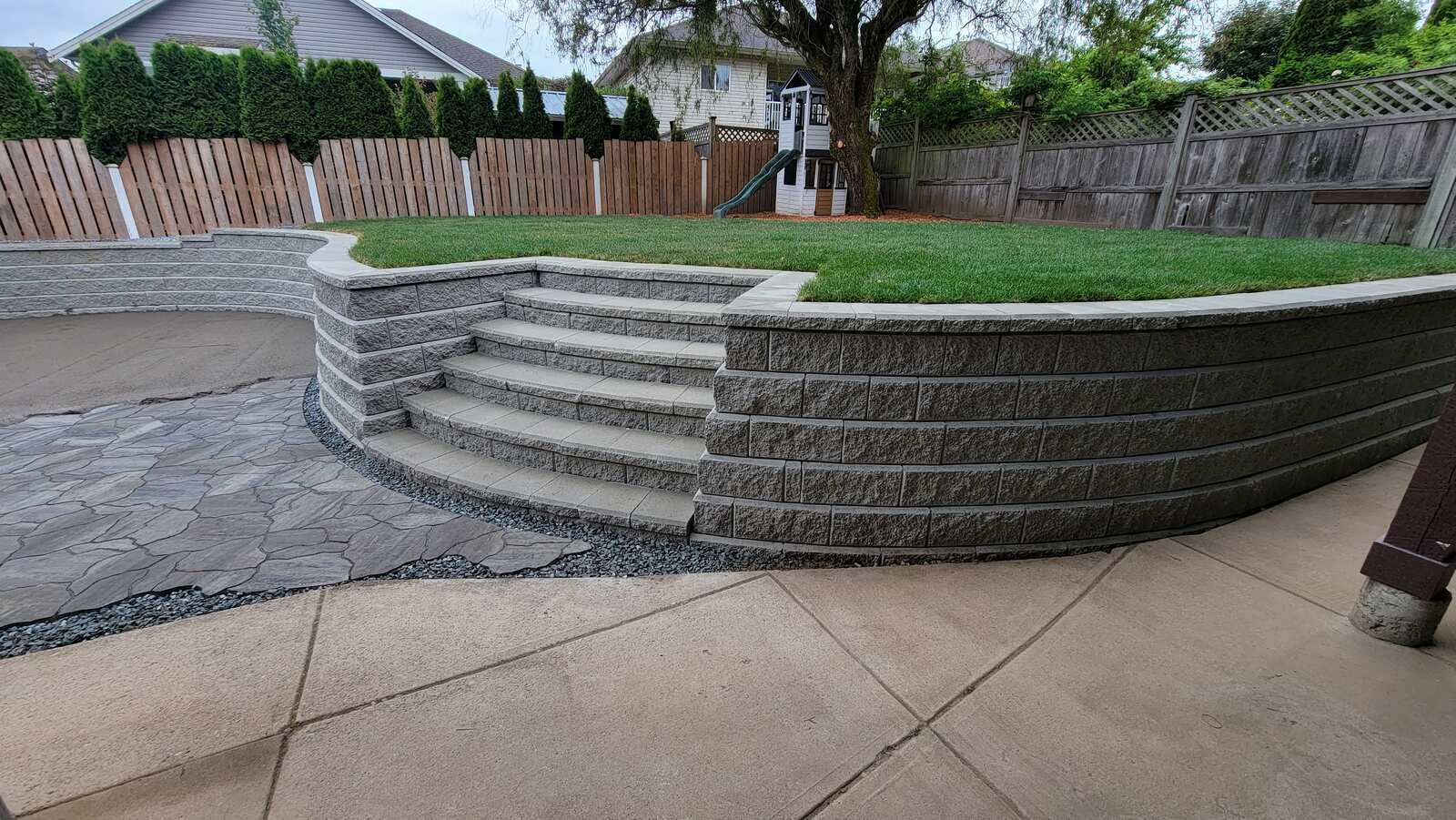 Patio with curved retaining wall and tiered stone steps by Back 40 Landscaping in Abbotsford, BC