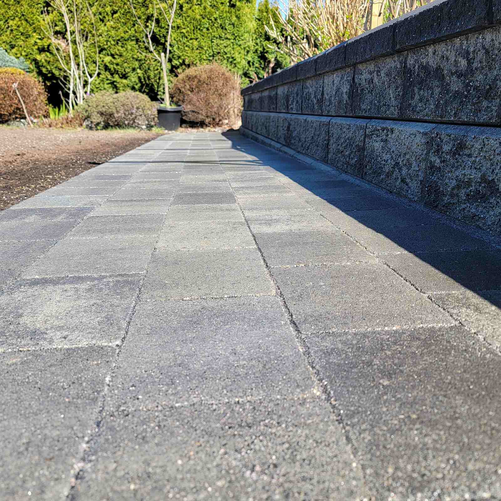 Low-angle view of paved pathway along stone retaining wall by Back 40 Landscaping in Burnaby, BC Low-angle view of paved pathway along stone retaining wall by Back 40 Landscaping in Burnaby, BC