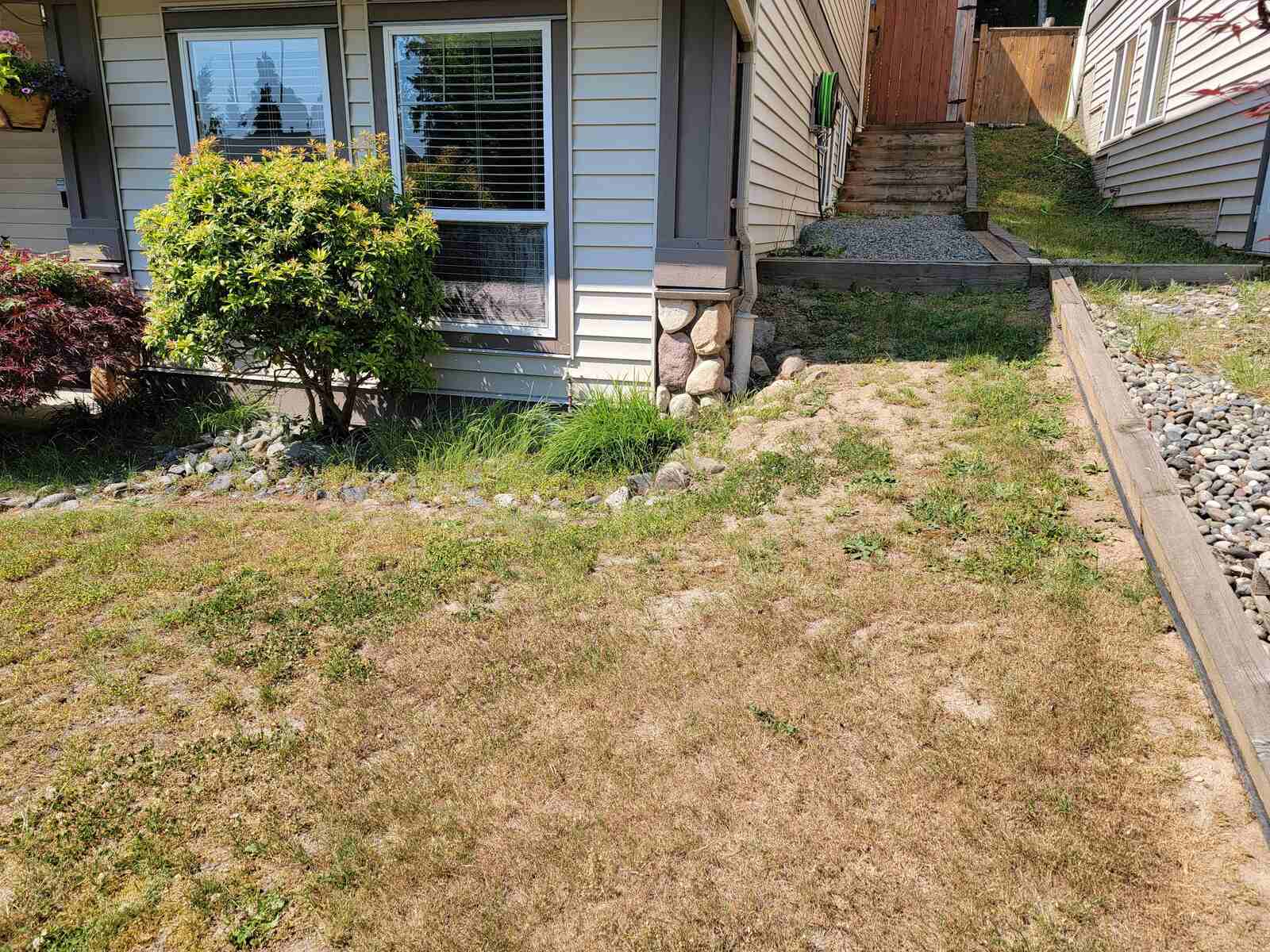 1_Four-tiered retaining wall project by Back40 Landscaping in Mission, BC, showing a front yard with overgrown grass and a windowed facade