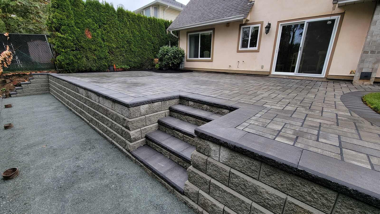 Elevated patio with gray pavers by Back 40 Landscaping in Abbotsford, BC, featuring steps leading to a well-defined terrace