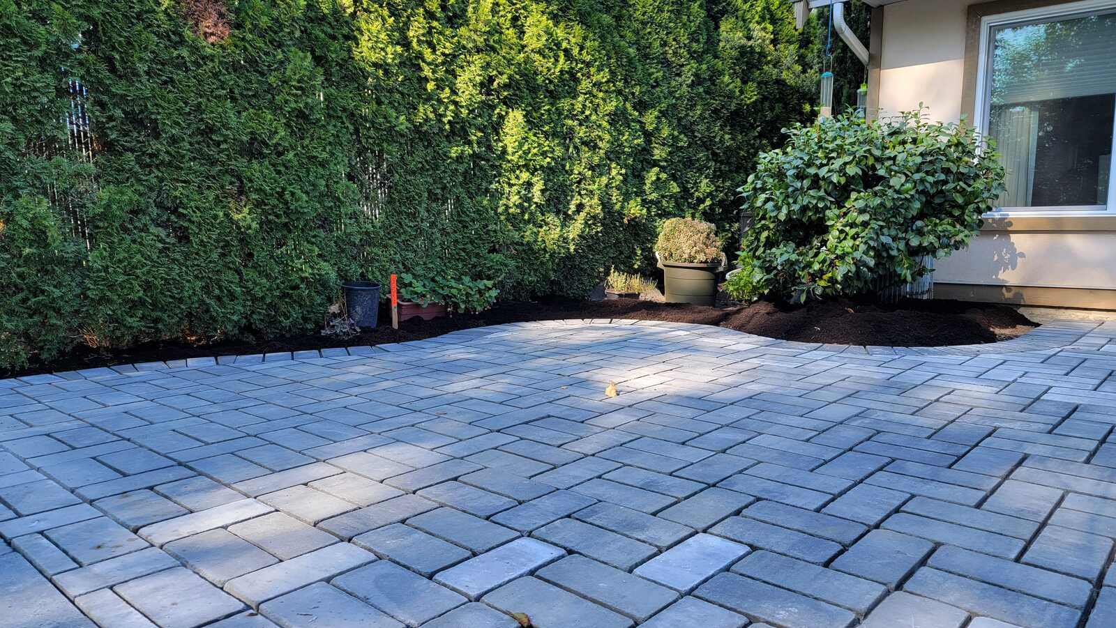 Close-up of newly installed patio against a green hedge by Back 40 Landscaping in Abbotsford, BC