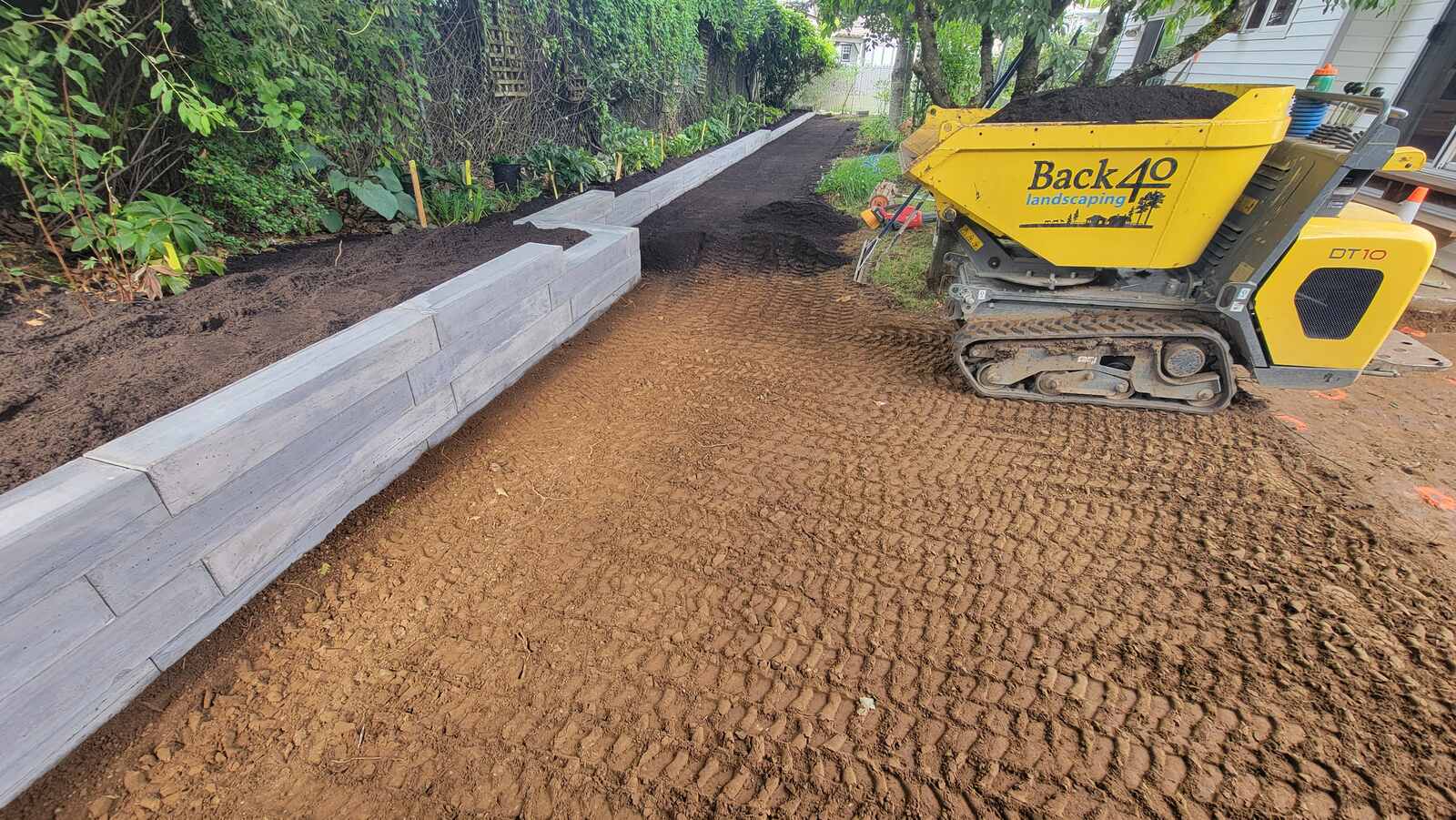 Back 40 Landscaping smoothing dirt path beside newly built concrete retaining wall in Abbotsford, BC