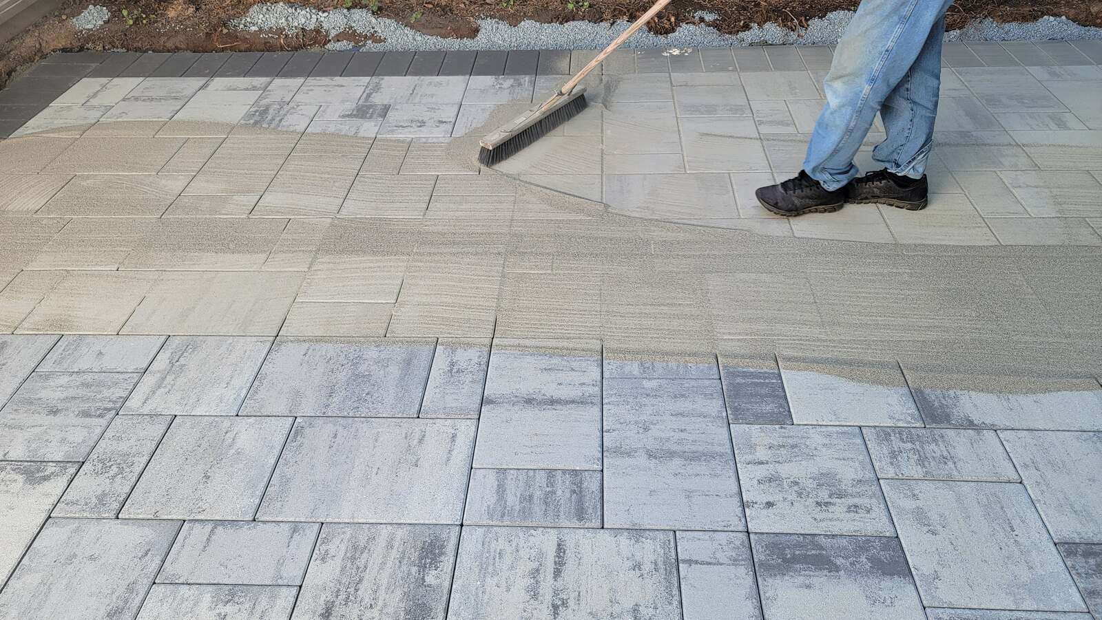 Worker spreading sand over concrete pavers in patio installation by Back 40 Landscaping, Abbotsford, BC