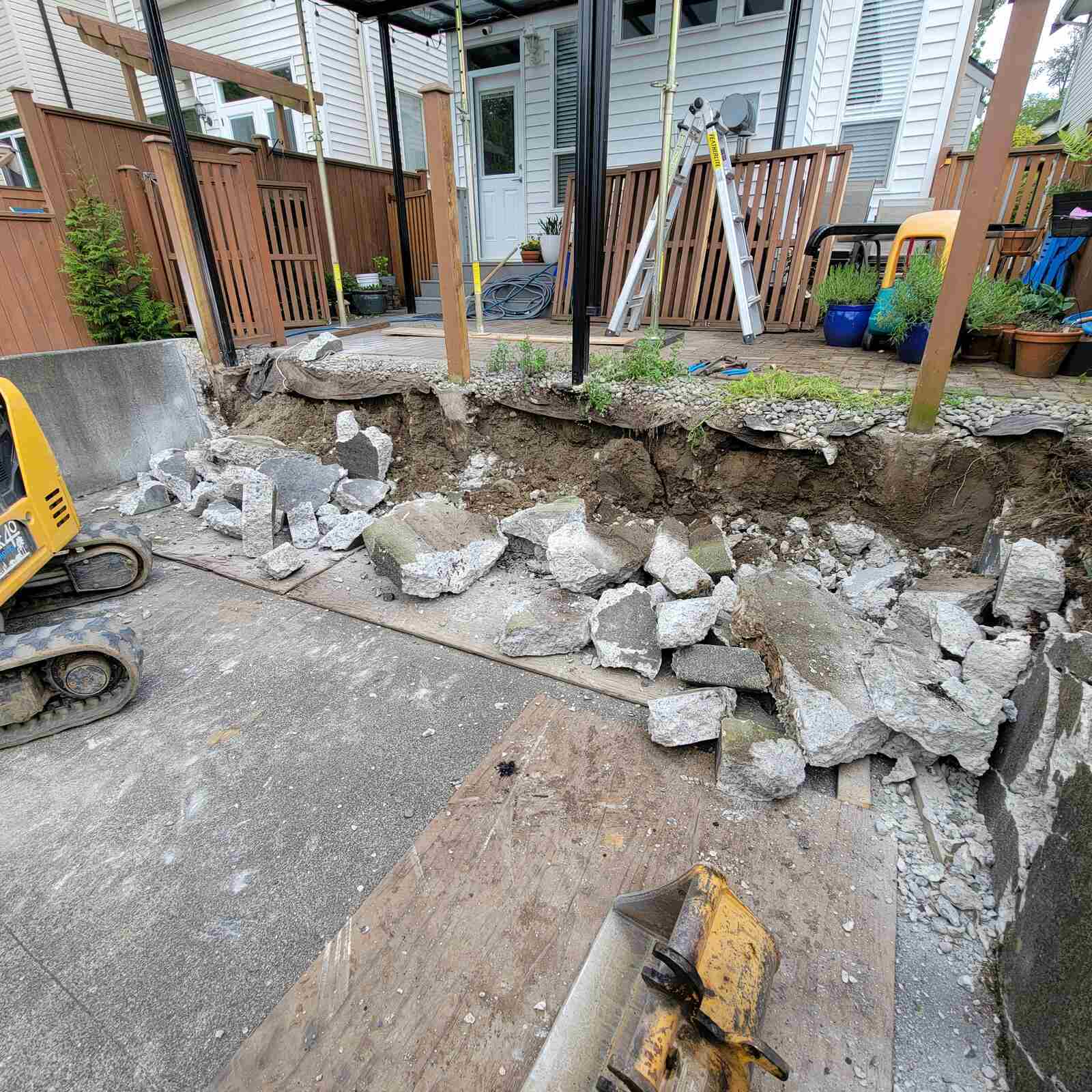 Construction equipment breaking down retaining wall in Langley, BC, by Back 40 Landscaping