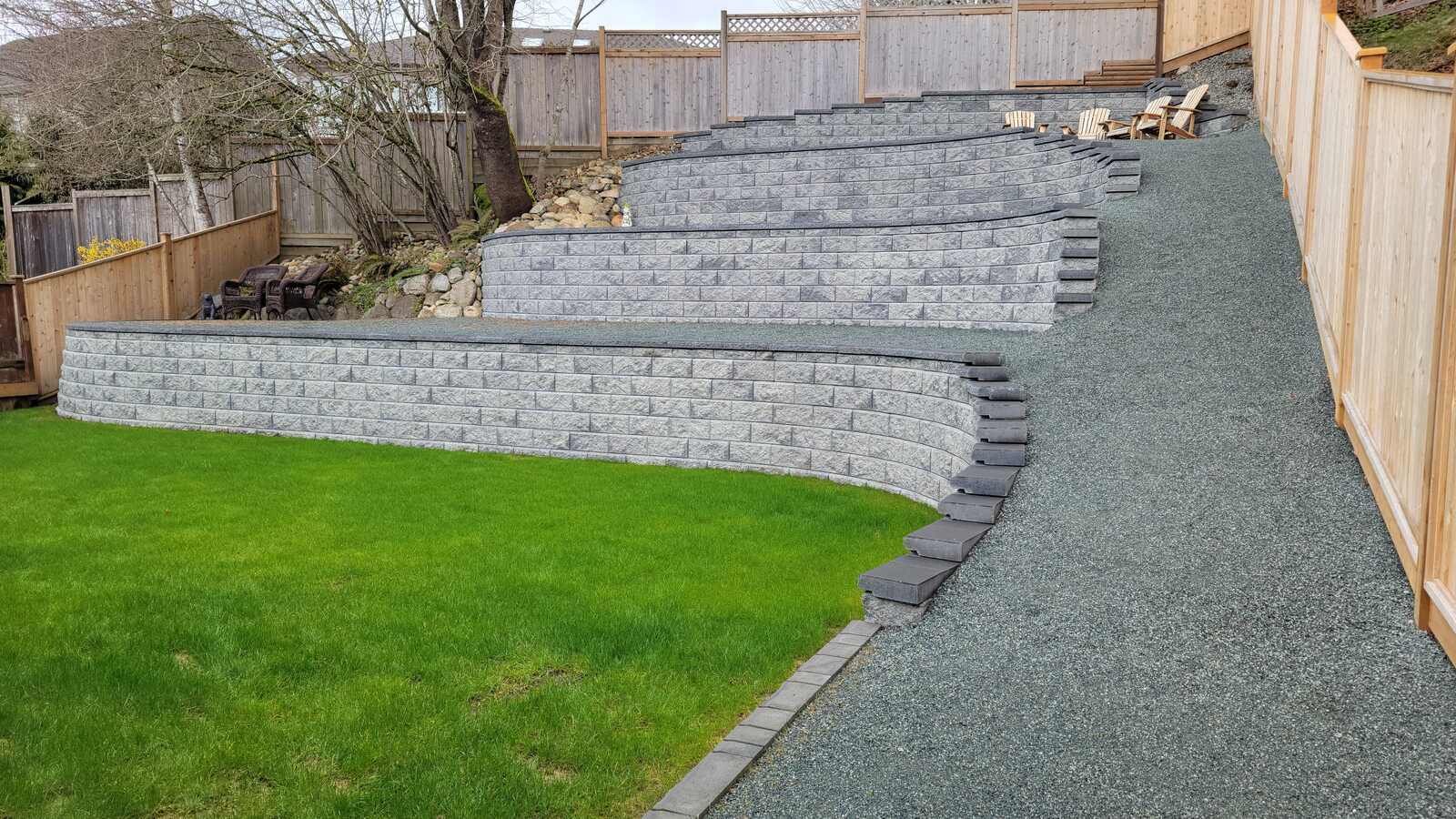 Lush green lawn beside a four-tier retaining wall in Langley, BC by Back 40 Landscaping