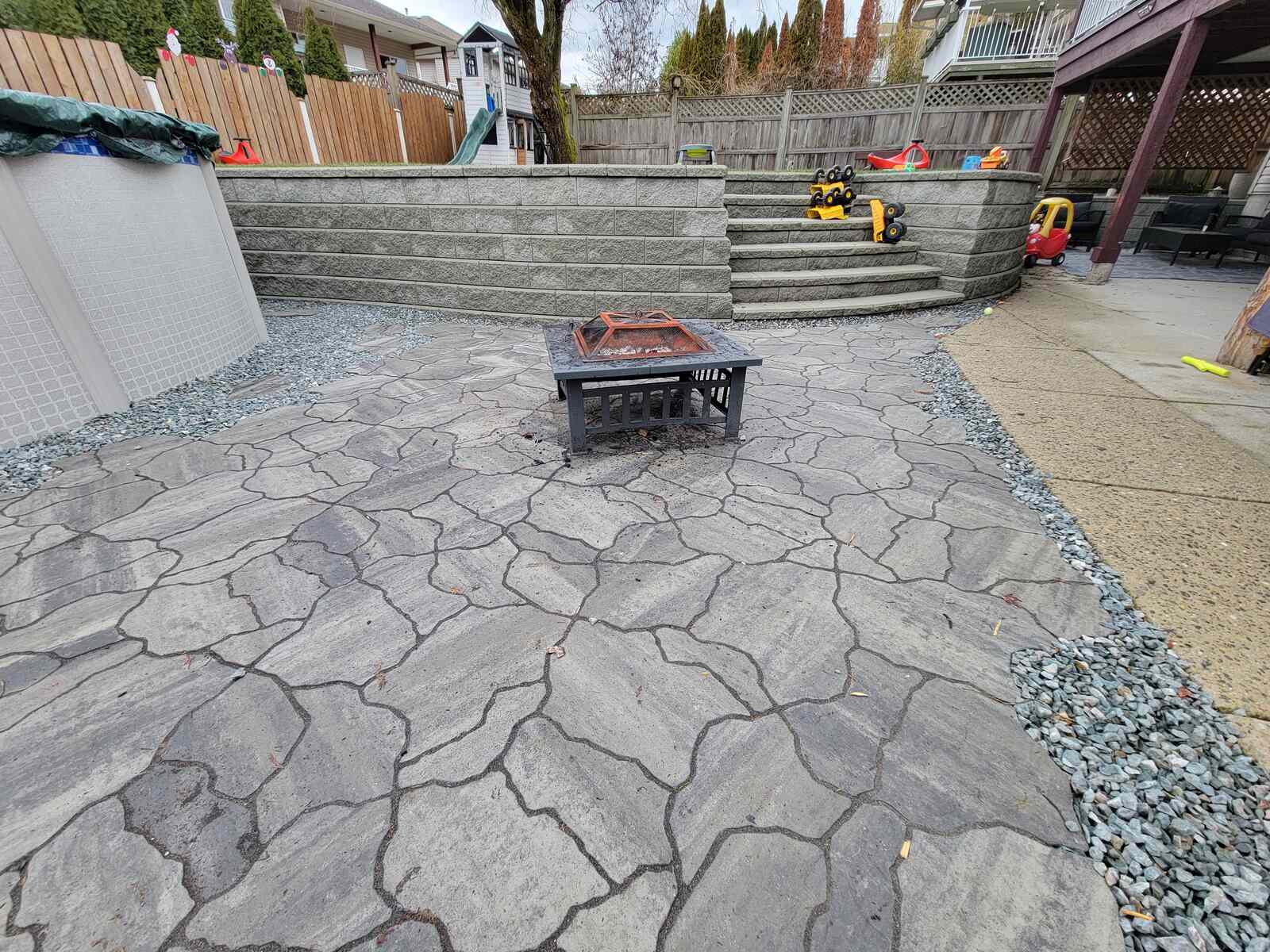 Flagstone patio with fire pit and above-ground pool by Back 40 Landscaping in Mission, BC