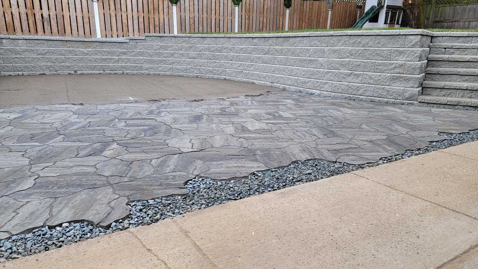 Stone patio with a curved retaining wall by Back 40 Landscaping in Abbotsford, BC, showcasing unique stone patterns