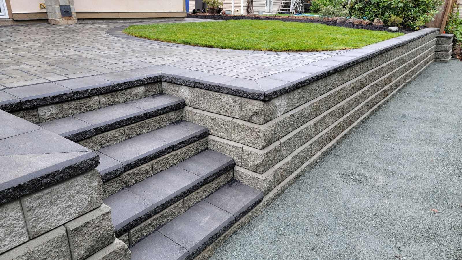 Retaining wall with stone steps by Back 40 Landscaping in Abbotsford, BC, showcasing layered pavers and green lawn